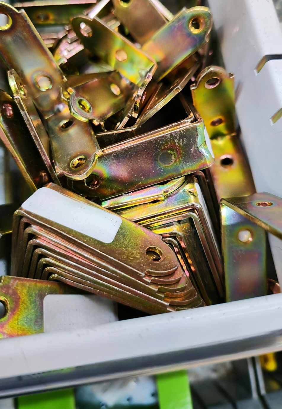 Pile of gold-colored metal brackets and hardware in a white bin