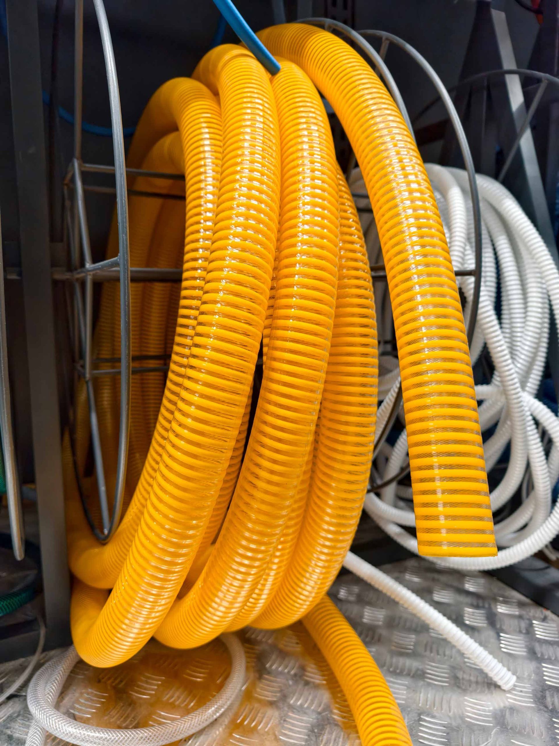 Coiled yellow and white corrugated hoses stacked on a wet floor in a utility area
