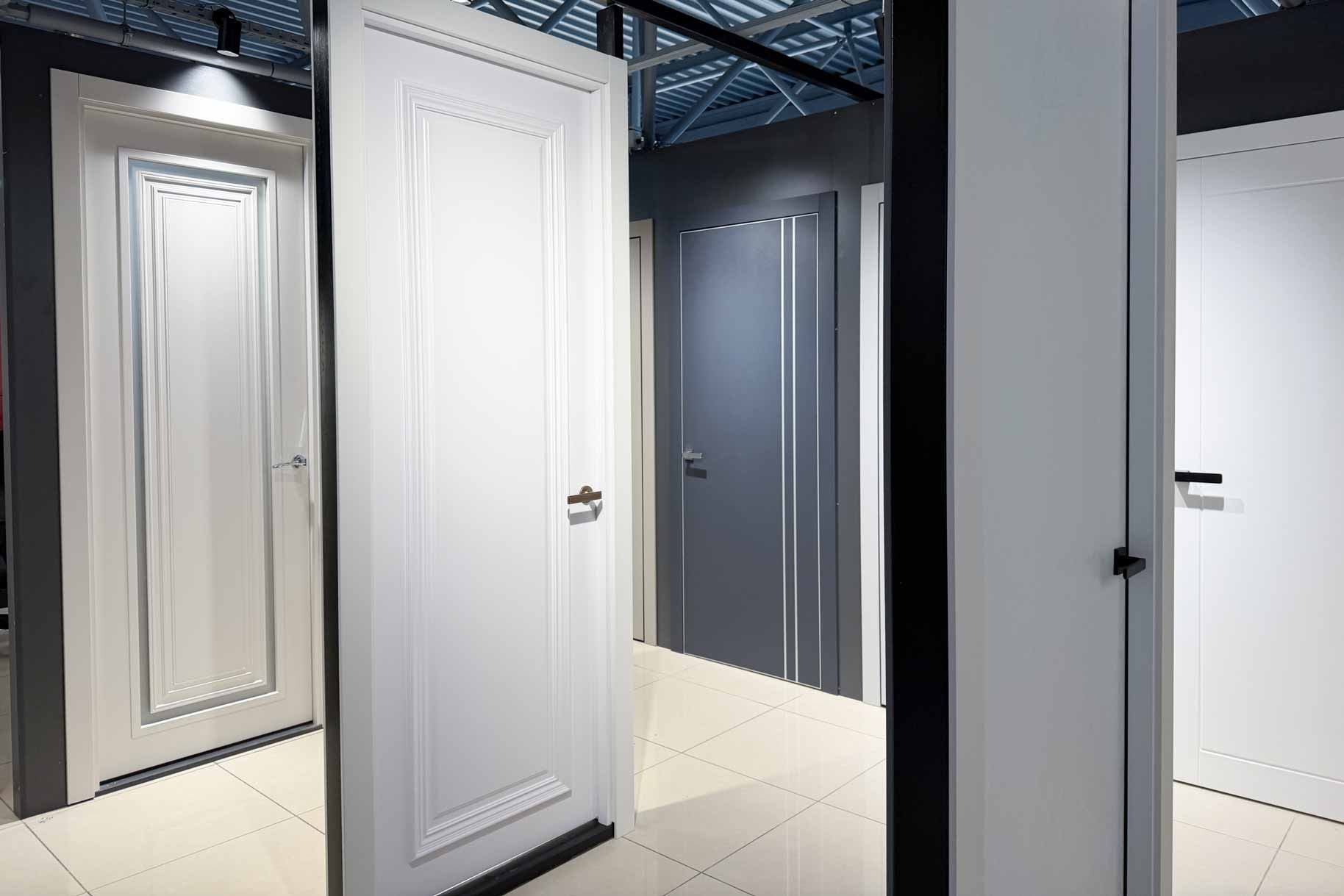 Interior hallway with multiple white doors and gray walls under industrial ceiling lighting