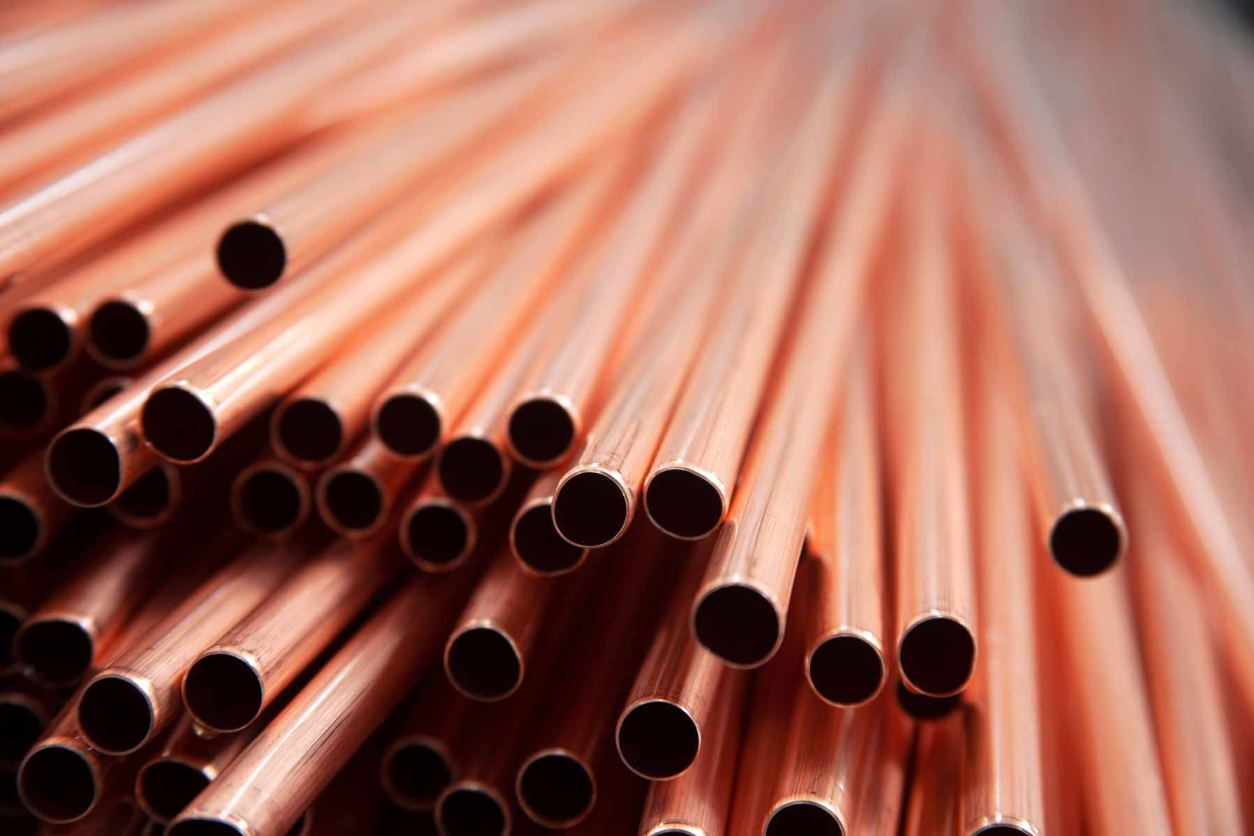 Close-up of stacked copper pipes with circular openings, arranged diagonally on a soft pink background