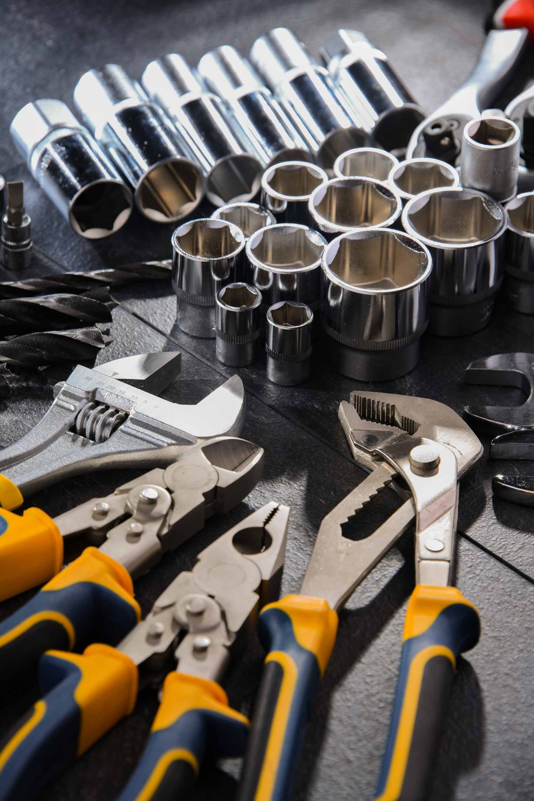 Assorted chrome sockets and pliers with blue-and-yellow handles on a dark workbench