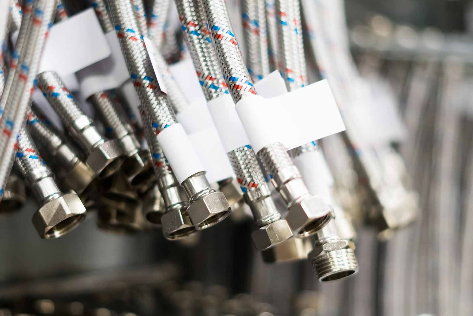 Close-up of braided metal hoses with threaded ends hanging in a row