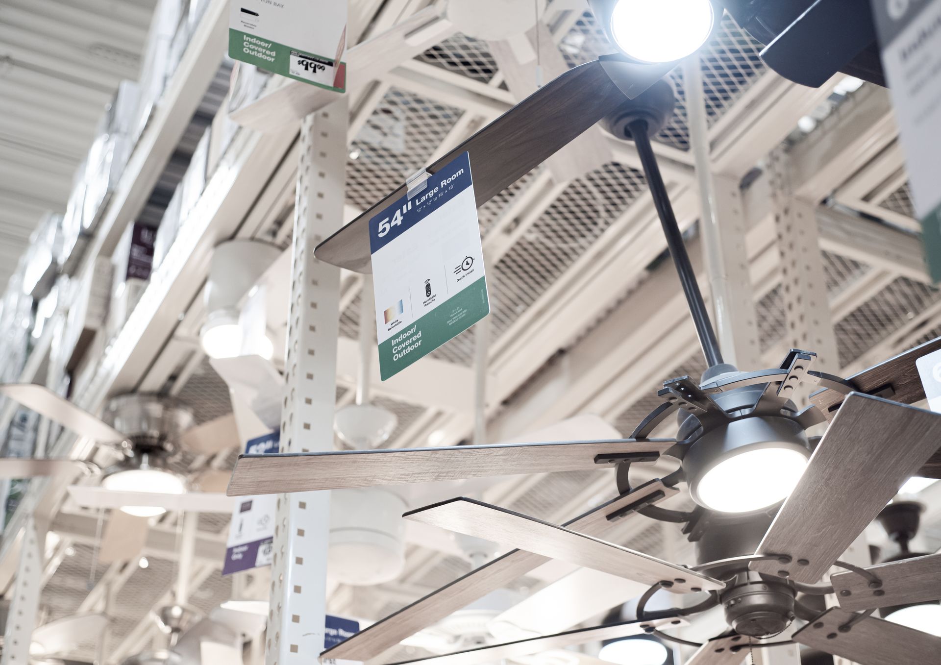 Ceiling fans displayed in a bright store aisle with hanging price signs