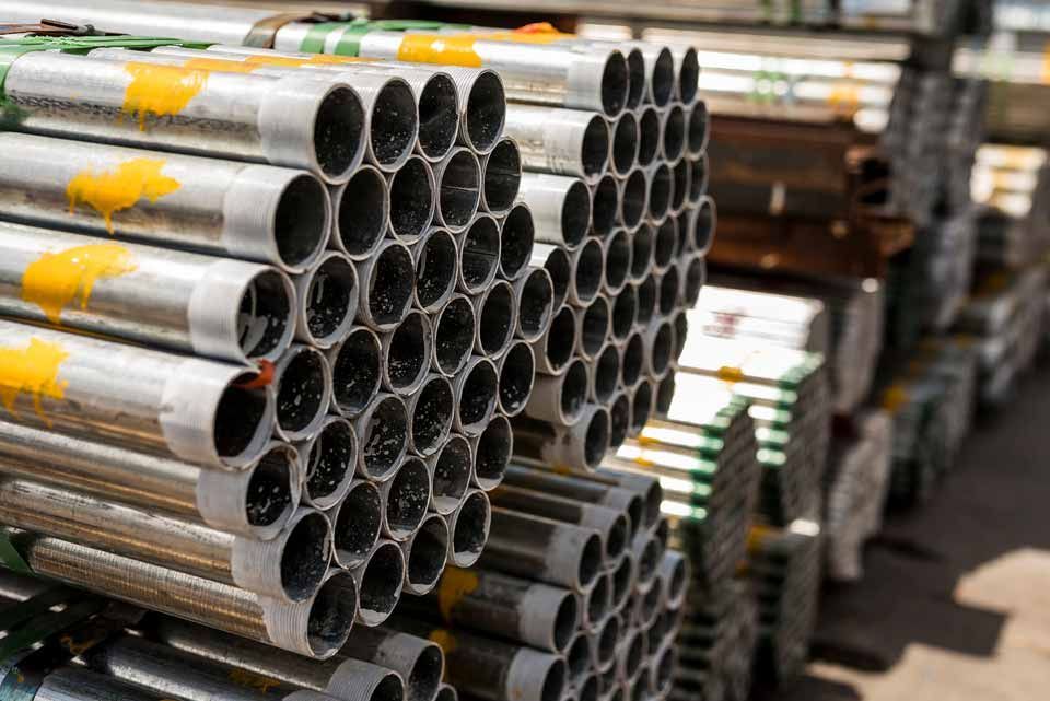 Stacked metal pipes in a warehouse, with silver ends facing forward.