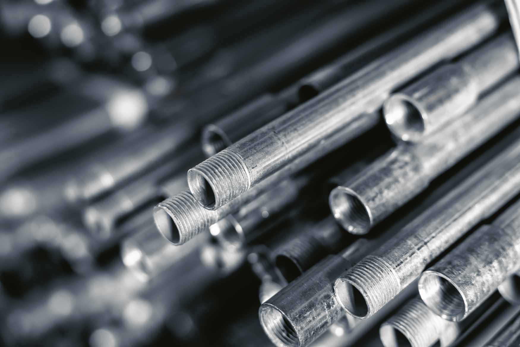 Stacked shiny metal pipes with threaded ends, seen in close-up.