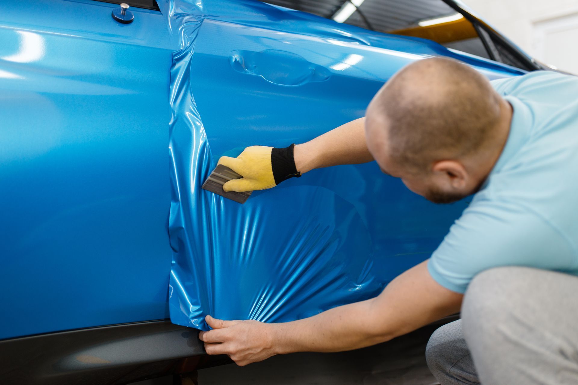 A man is wrapping a blue car with plastic wrap.