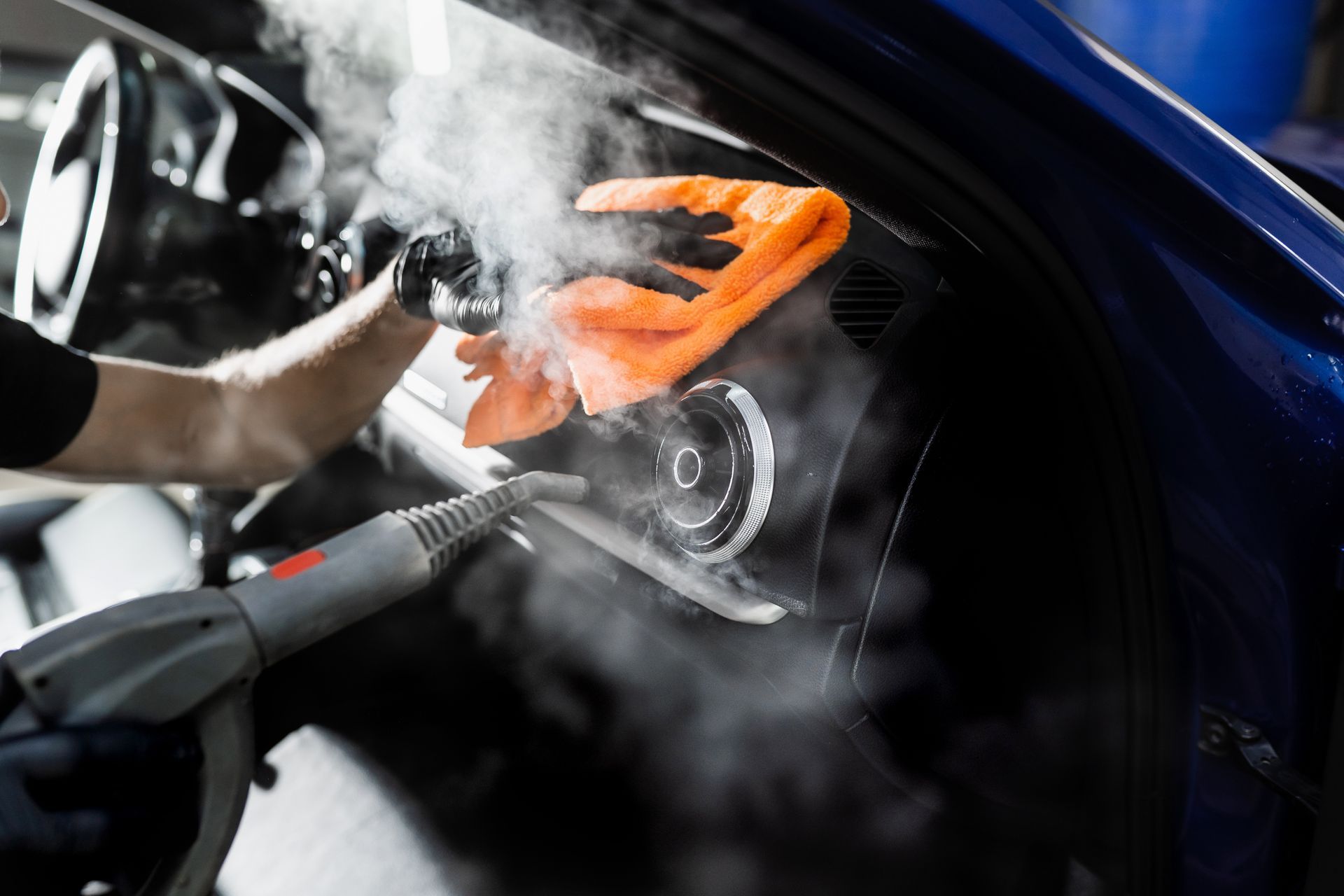 A person is cleaning the interior of a car with a steam cleaner.