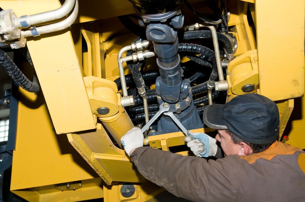 A Man Is Working On A Yellow Tractor With A Wrench — Wards Byron Shire Truck & Machinery Centre In Tyagarah, NSW