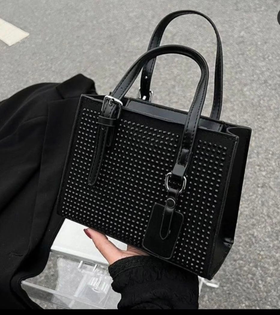 Una mujer sostiene un bolso negro con tachuelas.