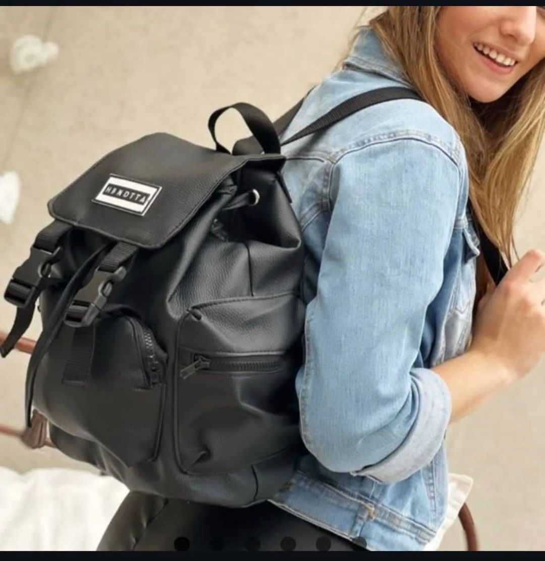 Una mujer con una chaqueta vaquera lleva una mochila negra.