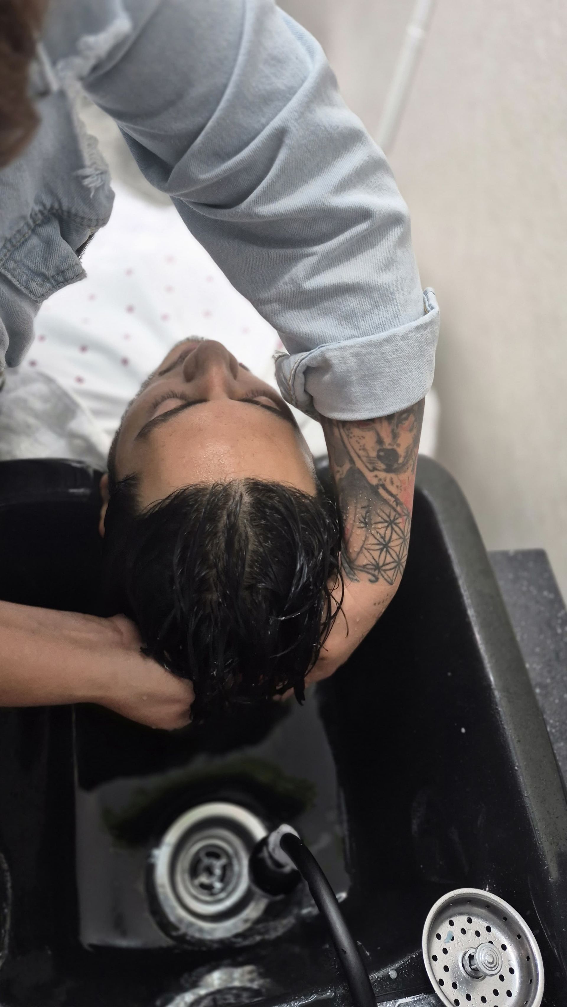 Person having hair washed in a salon sink by a person with tattoos on their arm.