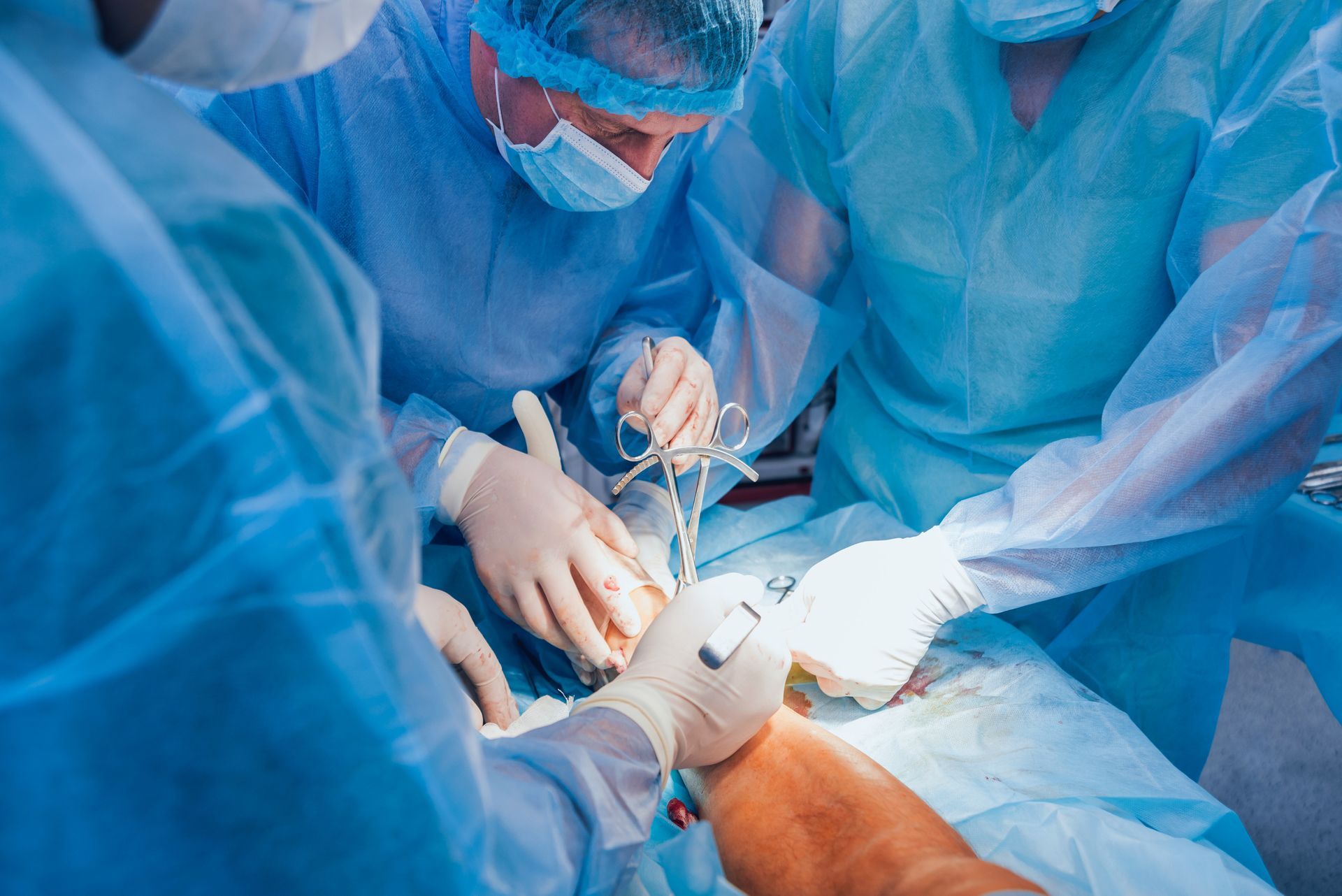 Surgeons in blue scrubs perform surgery on a patient, with surgical instruments.