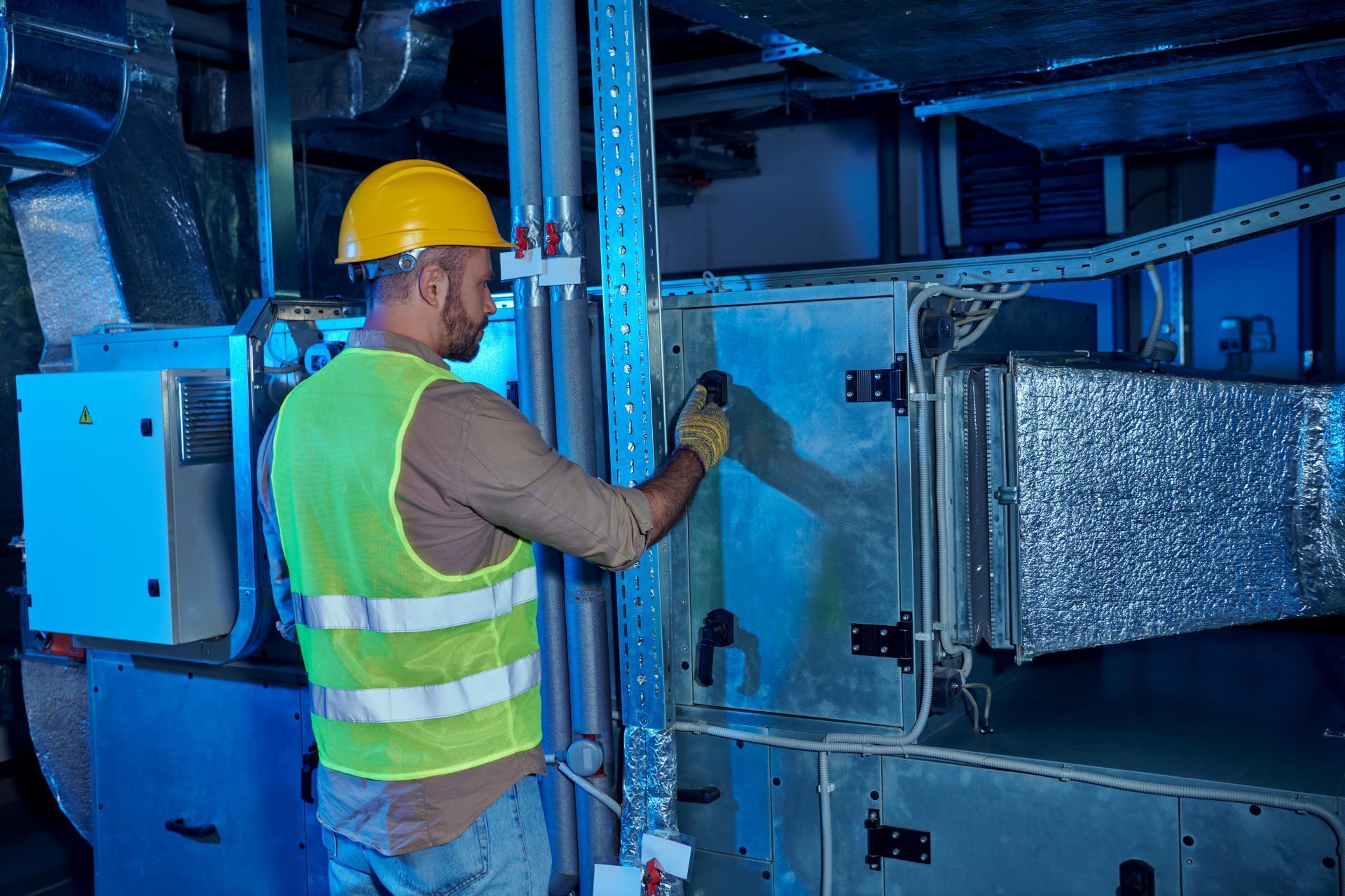 A man wearing a hard hat and safety vest is working on a machine in a factory.