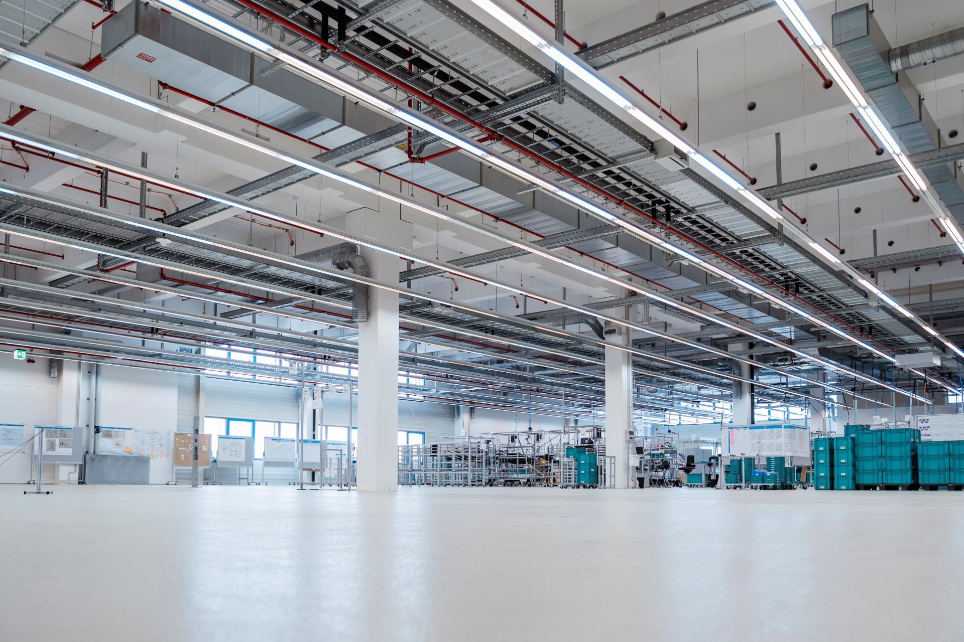 Illuminated warehouse of modern factory with high ceiling ductwork and lights and pillar beams going to the floor.