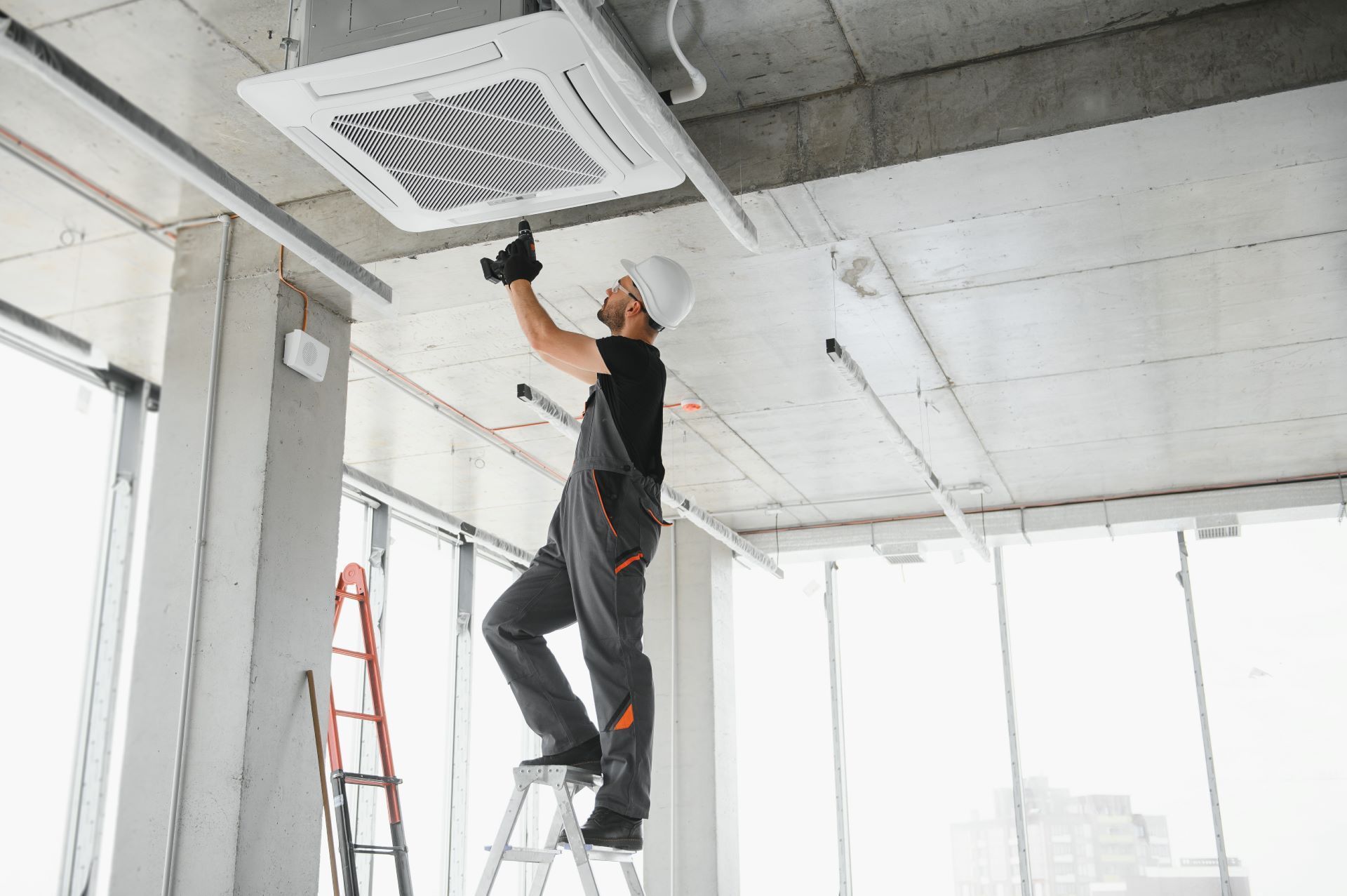 A man is standing on a ladder working on a ceiling fan.