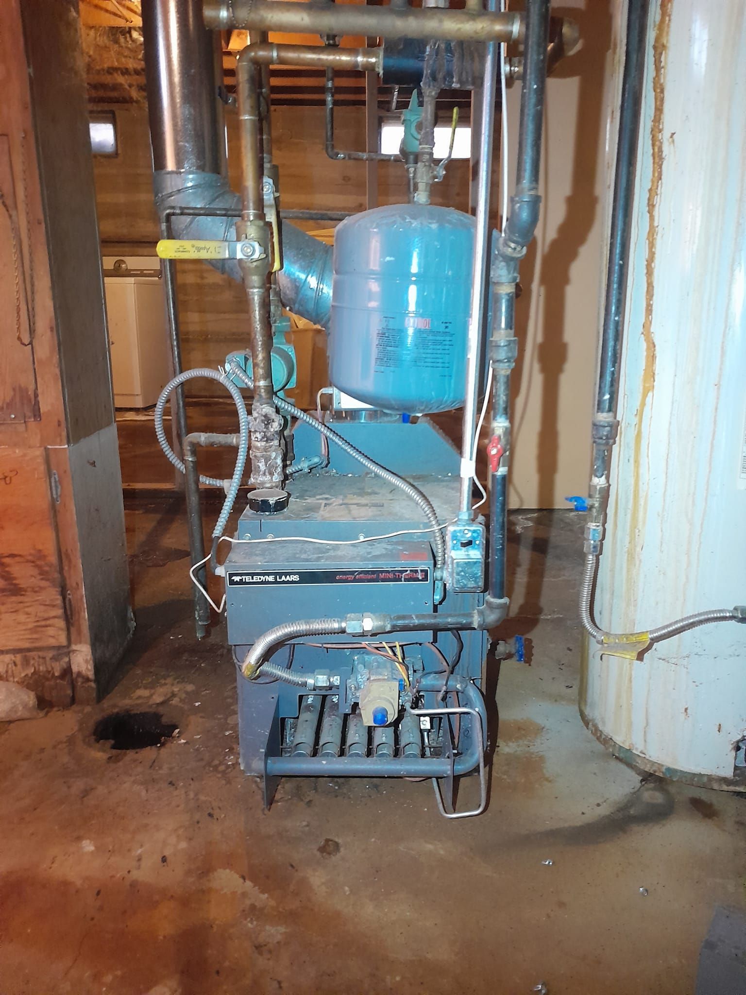 A blue boiler is sitting in a basement next to a white water heater.