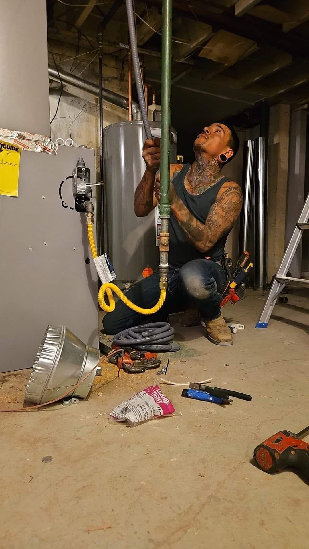 A man is working on a water heater in a basement.