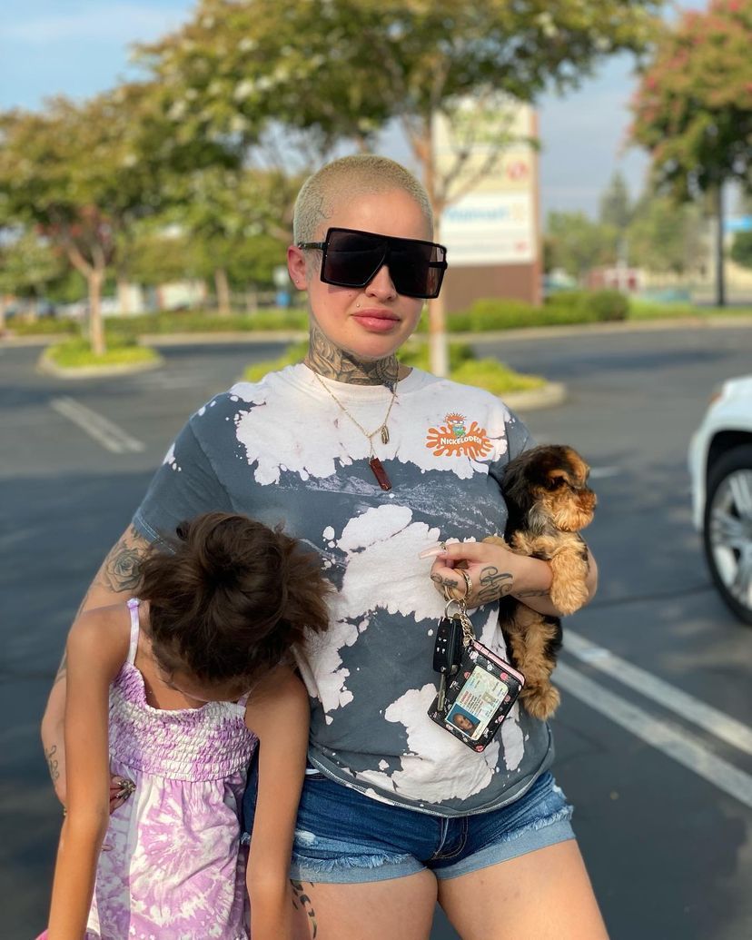 A woman wearing sunglasses is holding a puppy and a little girl.