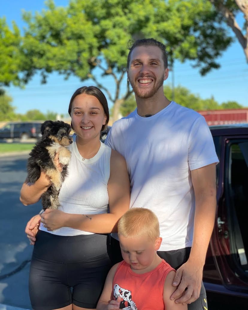 A man and woman holding a dog and a boy standing next to a car