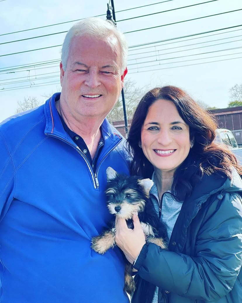 A man and a woman are posing for a picture while holding a small dog.