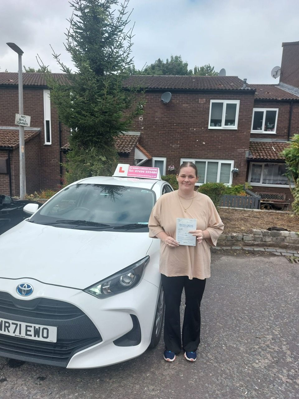Woman holding driving license stands next to white car with learner plate.