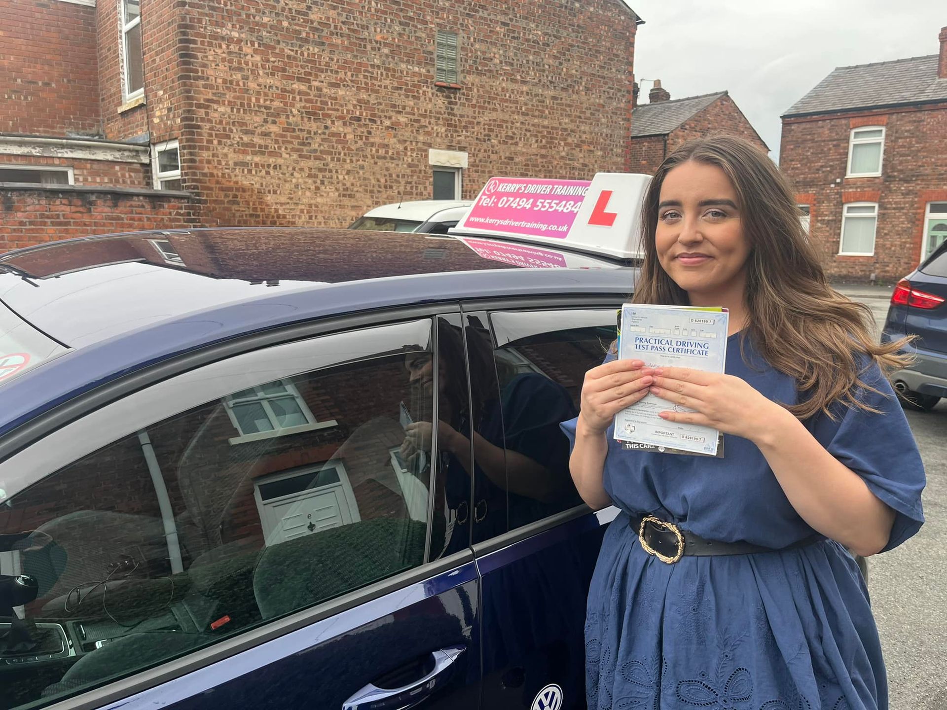 a woman in a blue dress is standing in front of a car holding a certificate .