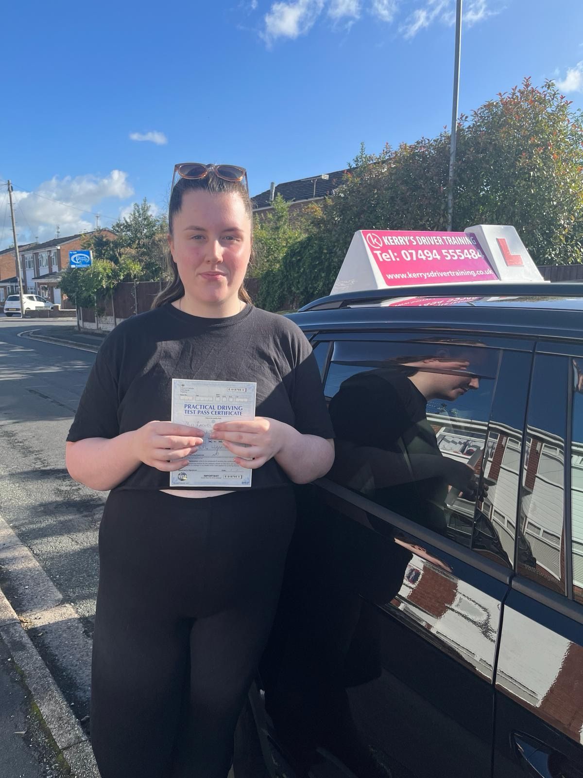 a woman is standing next to a car holding a driving license .