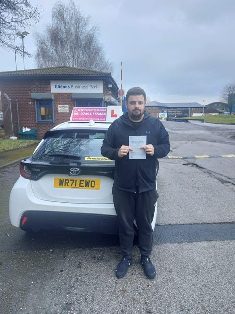 A man is standing in front of a white car holding a driving license.