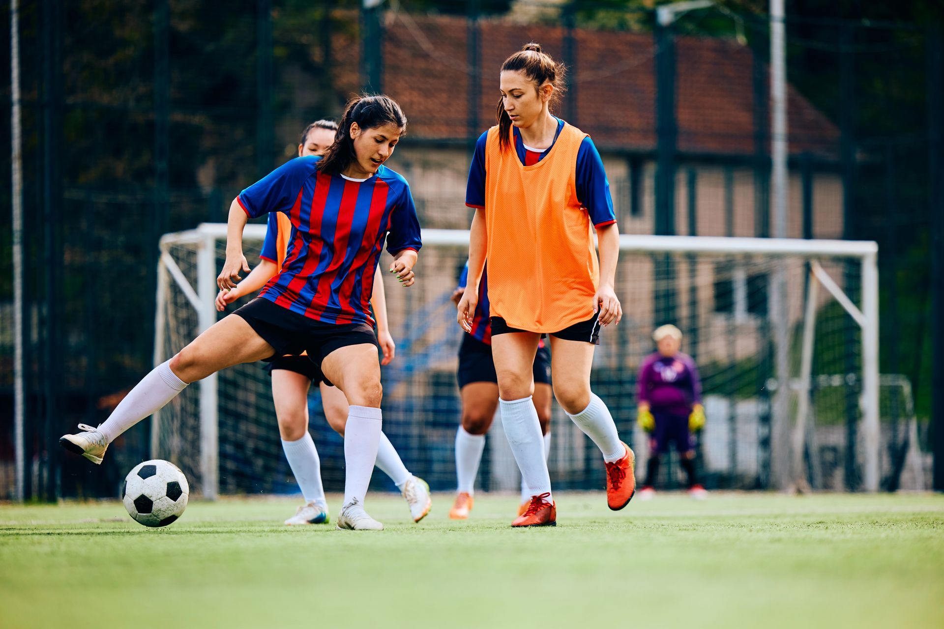 Women playing soccer on a green field. One kicks the ball, others watch.