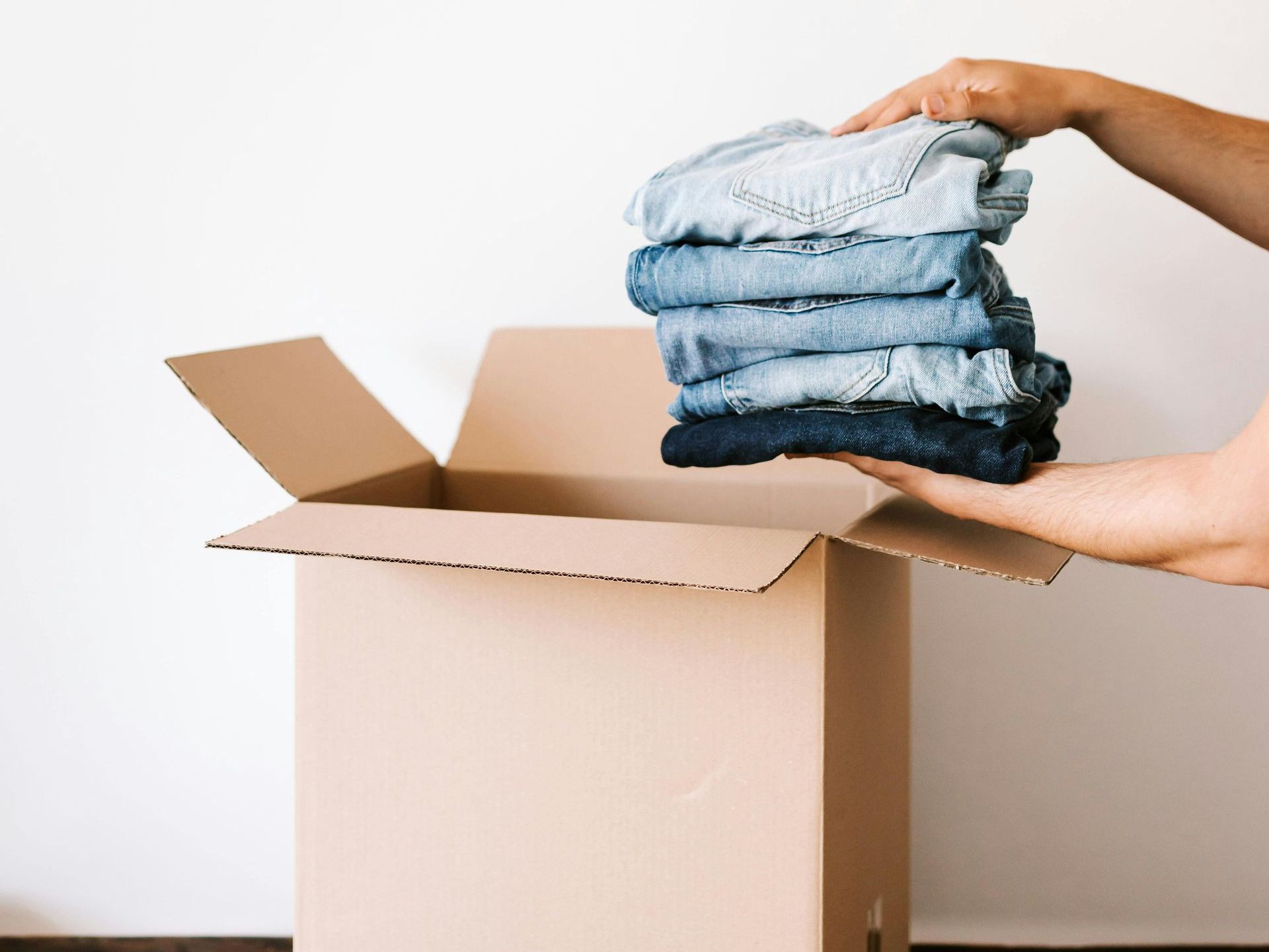 A person is holding a stack of clothes out of a cardboard box.