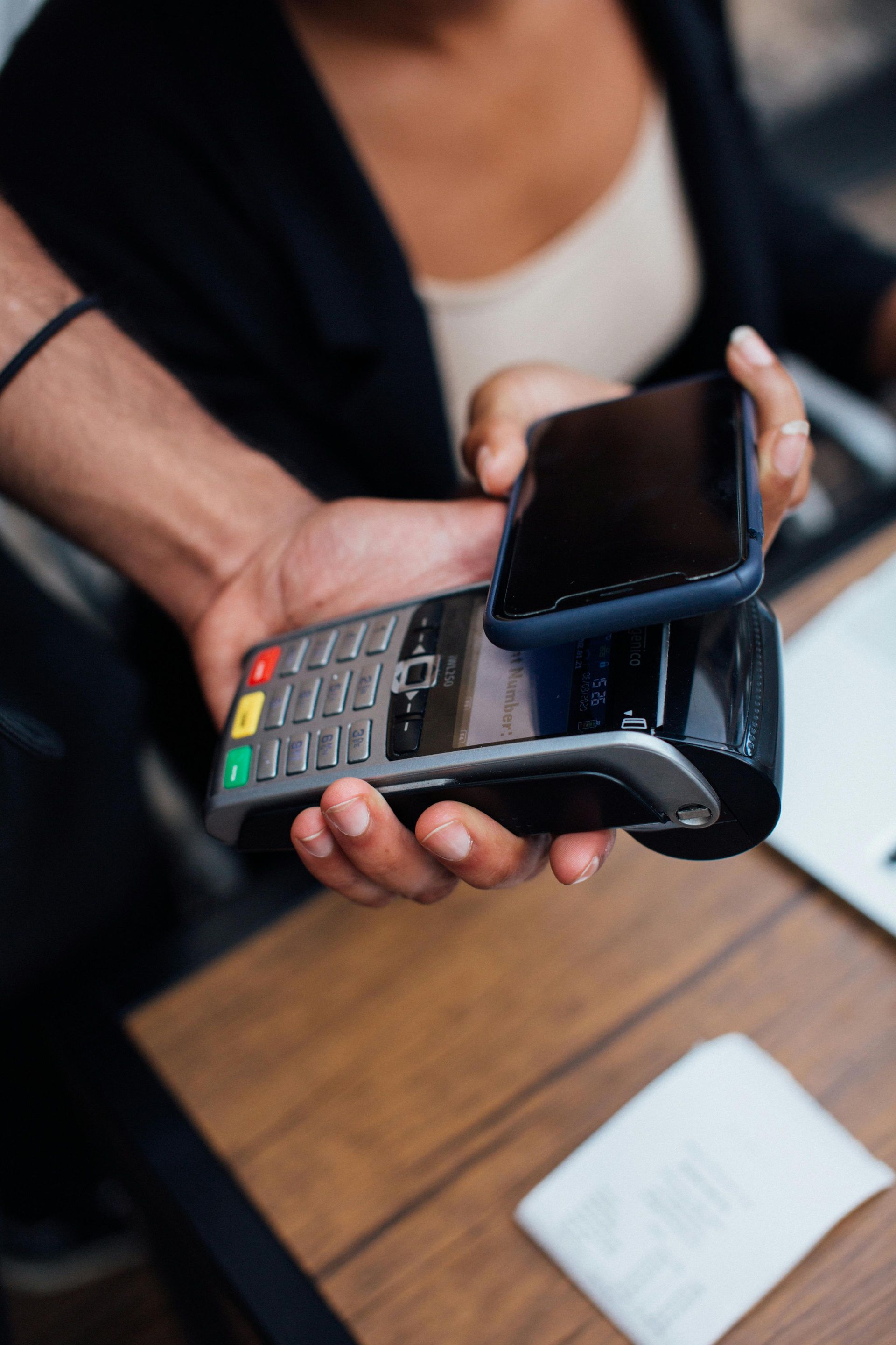 A woman is holding a cell phone over a credit card machine.