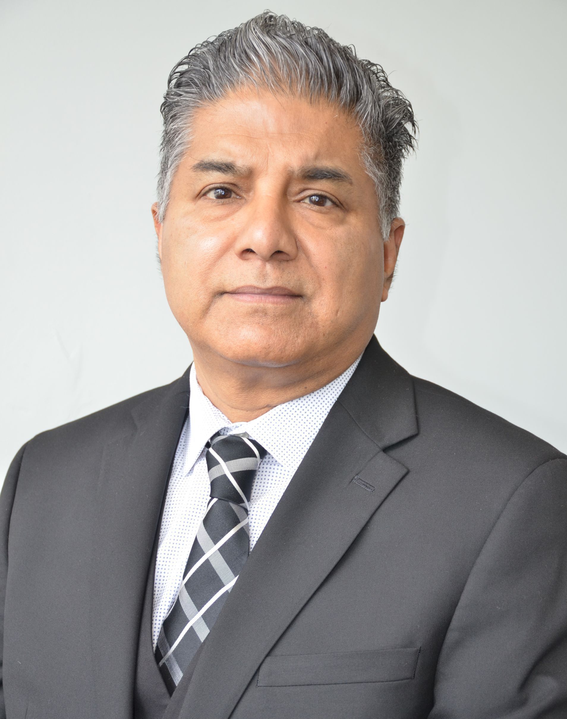 Man in a suit and tie, looking forward, neutral expression, indoors, professional setting.