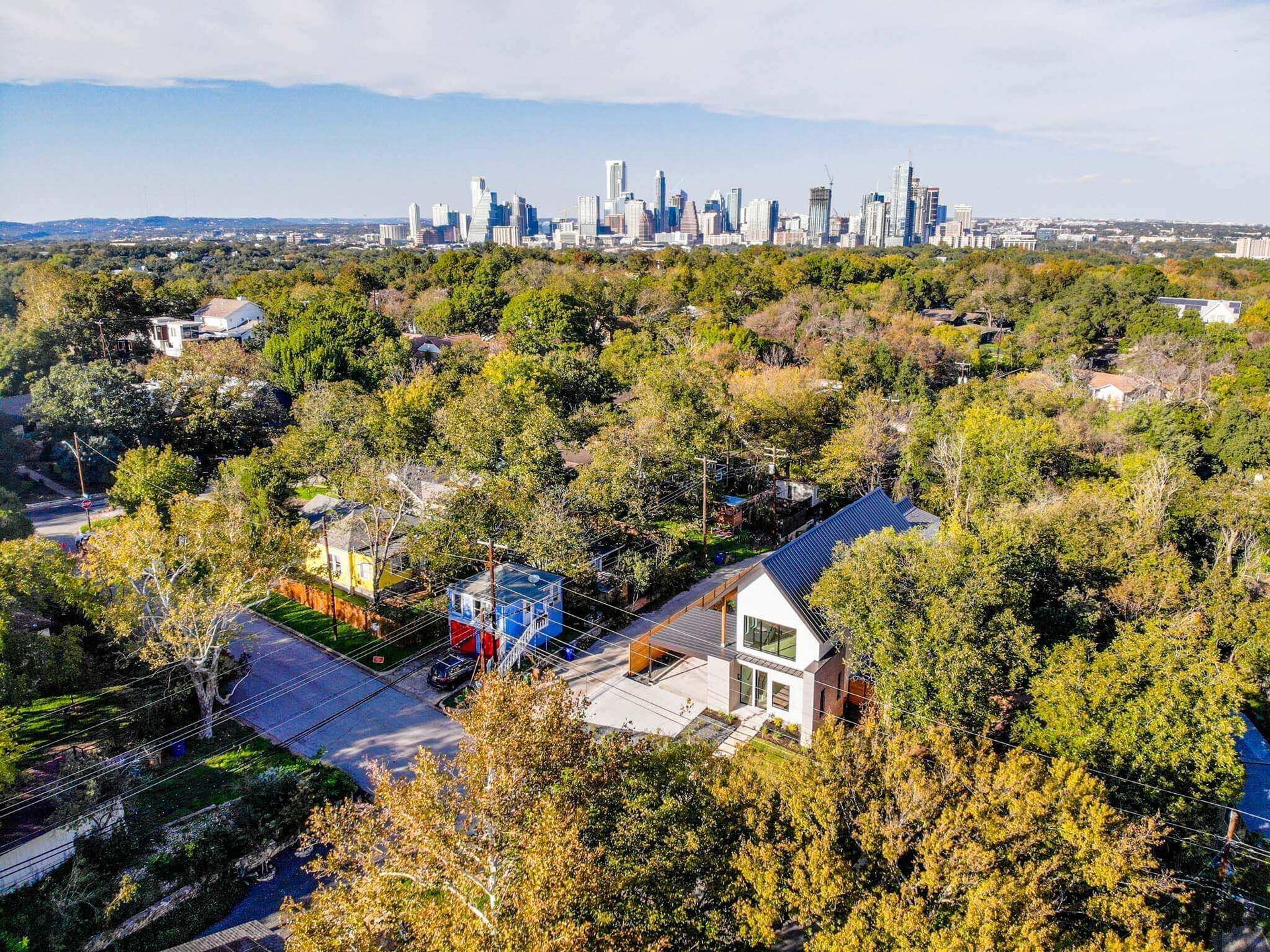 an aerial view of a house in the middle of a forest with a city skyline in the background .