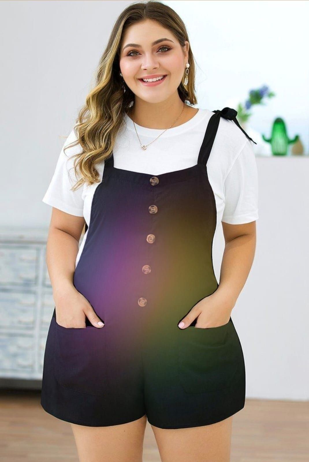 Mujer que viste pantalones cortos negros sobre una camiseta blanca, sonriendo y con las manos en los bolsillos.