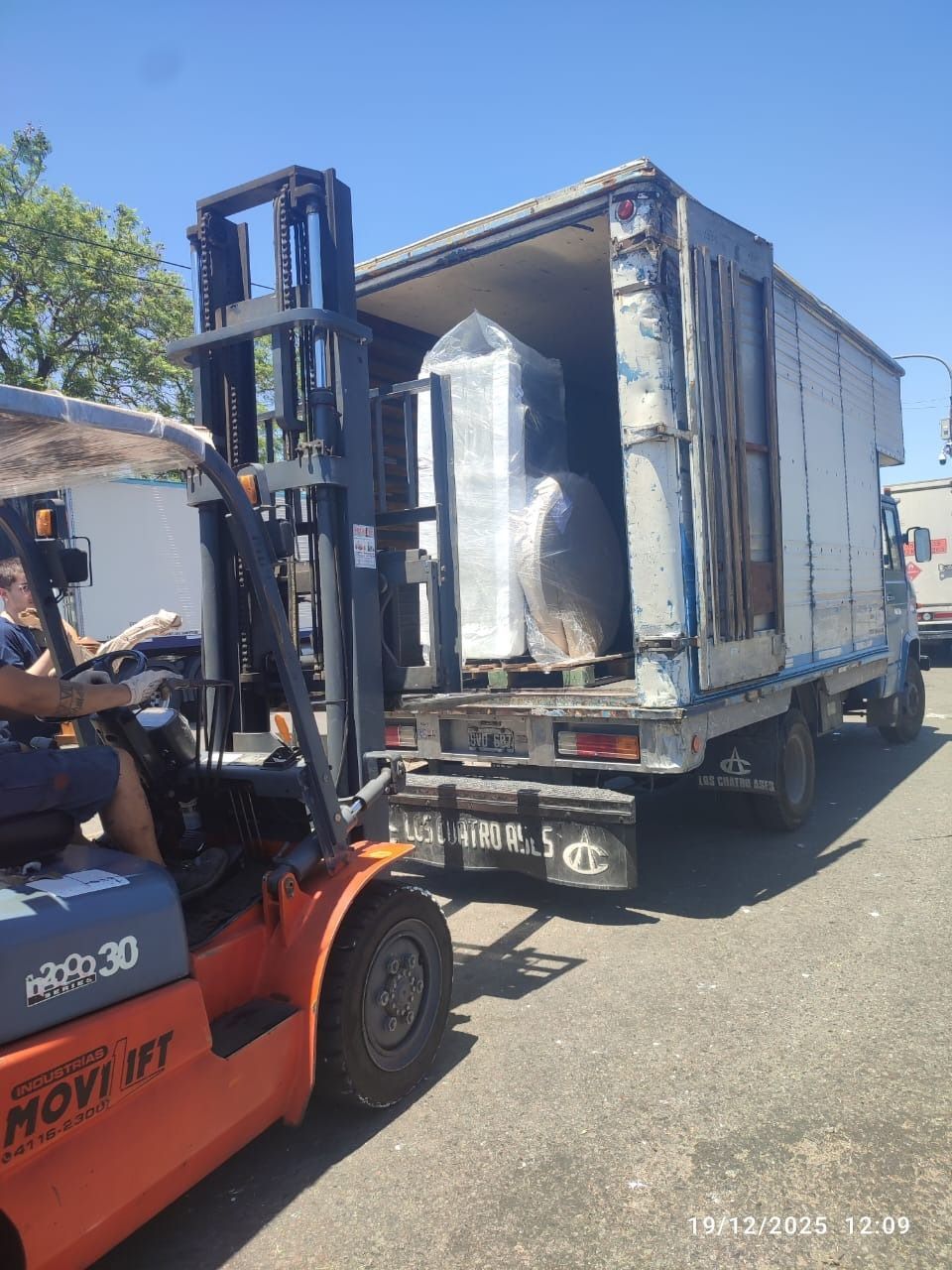 Carretilla elevadora cargando objetos envueltos en la parte trasera de un camión en un día soleado.