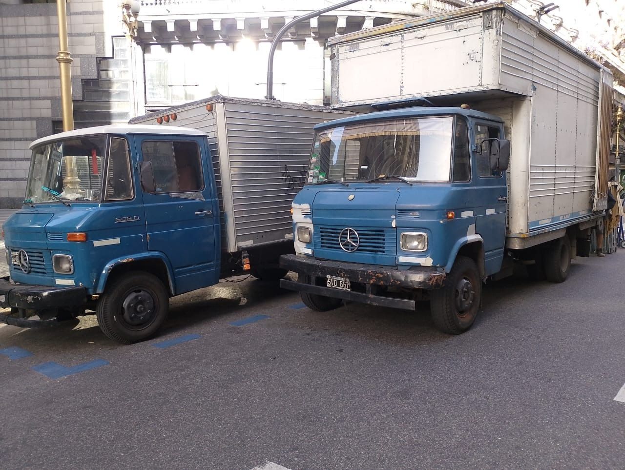 Dos camiones Mercedes-Benz azules estacionados en una calle de la ciudad.