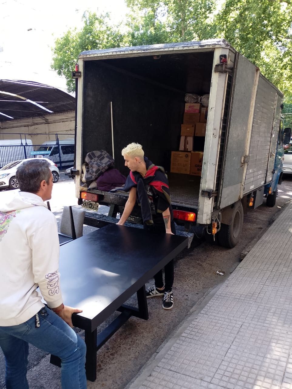 Dos personas cargan una gran mesa negra en un camión de mudanzas en una calle de la ciudad.