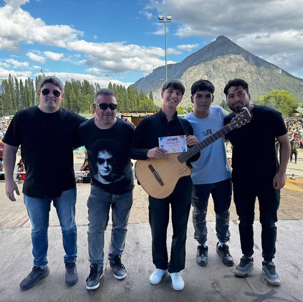 Cinco personas posando con una guitarra y un certificado al aire libre, con fondo de montañas.