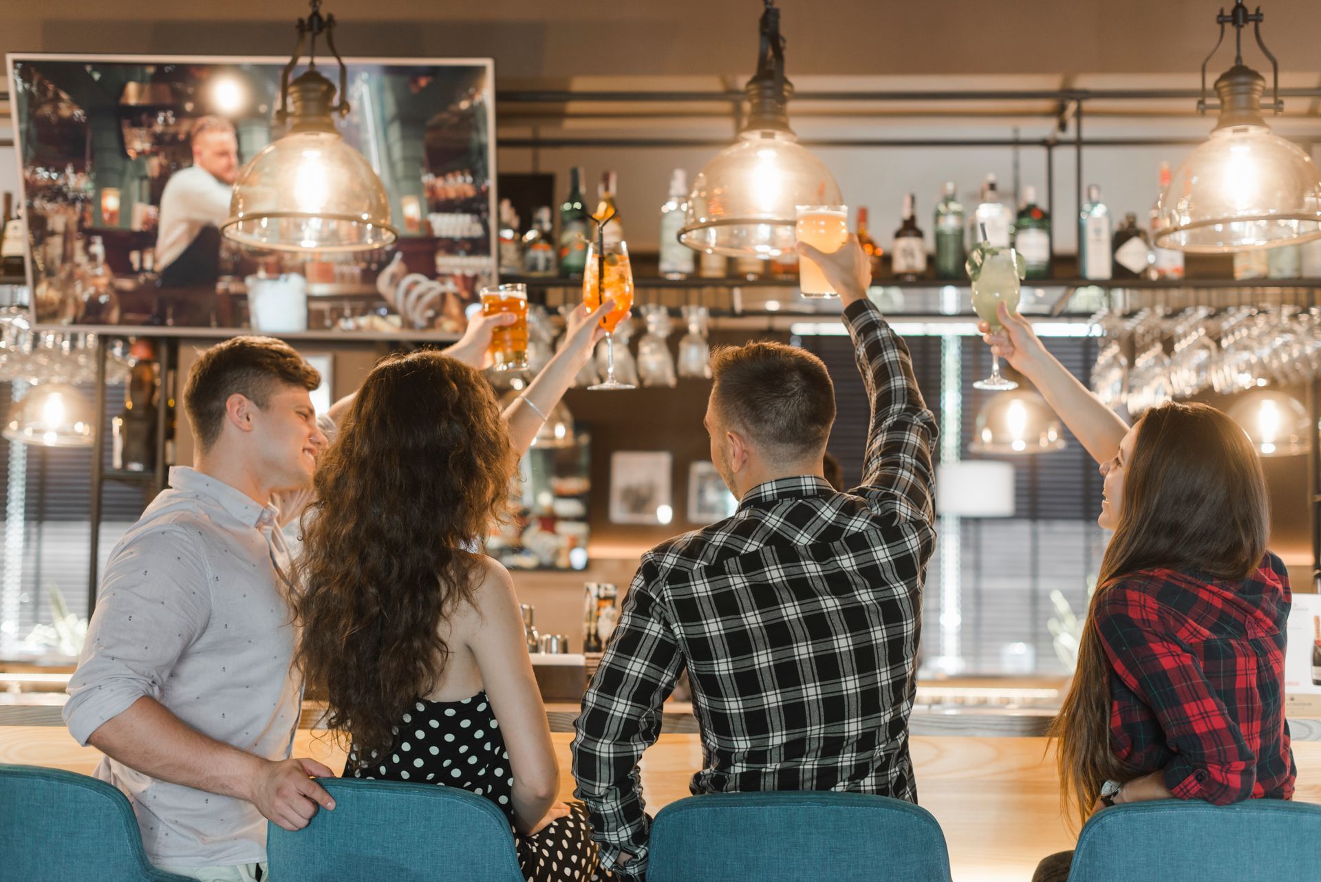 Cuatro personas brindando con bebidas en un bar, iluminado por lámparas de techo.
