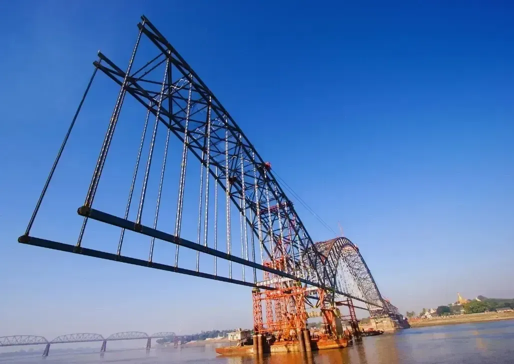 Unfinished steel bridge with exposed girders against a clear blue sky