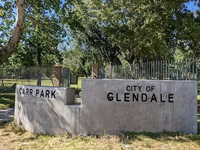 Carved stone marker reading 'Carr Park • City of Glendale' surrounded by lush grass and mature shade trees