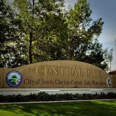 Weathered stone monument reading 'Central Park' with carved floral motifs, standing proudly amid lush greenery under sunny skies
