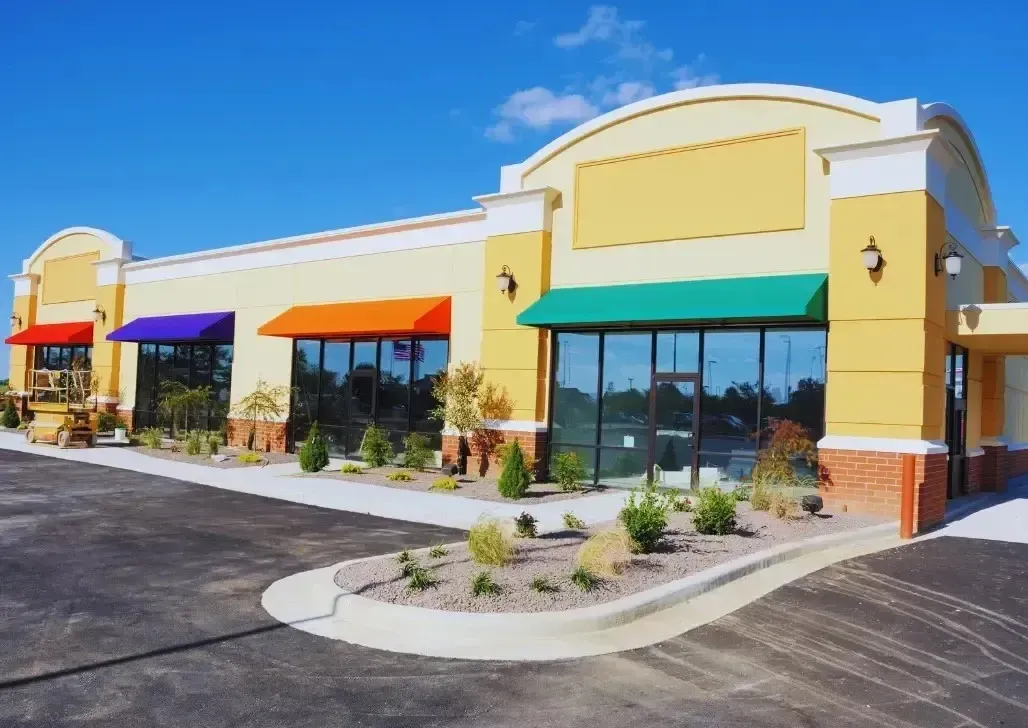 Bright yellow commercial building under blue sky with a colorful shed in front