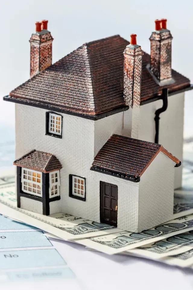 Hard Money Lender Los Angeles - A model house with a detailed roof and chimneys placed atop a stack of dollar bills, symbolizing real estate investment.