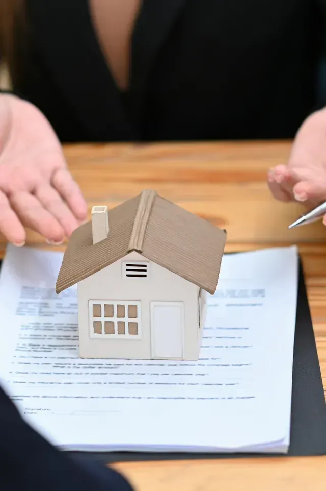 Hard Money Lender Los Angeles - A miniature house sits on paperwork, while a person gestures expressively during a real estate discussion.