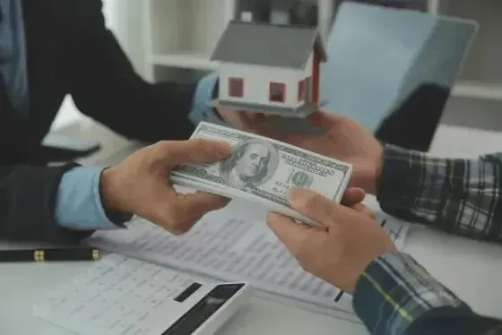 Hard Money Lender Los Angeles - A transaction is taking place between two individuals, where one is handing over a significant amount of money, likely cash, to another person in exchange for a model house.