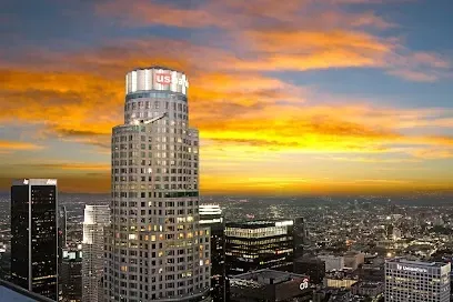 OUE Skyspace observation deck at sunset, with panoramic views of Los Angeles city lights under a vibrant orange-and-pink sky