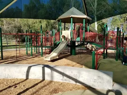 Shaded playground at Summit Park with modern play structures under large canopy trees, children climbing on a jungle gym while parents relax on nearby benches