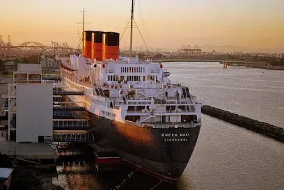 Historic RMS Queen Mary ocean liner docked in Long Beach, silhouetted against a vibrant sunset with orange and purple skies reflecting on the water