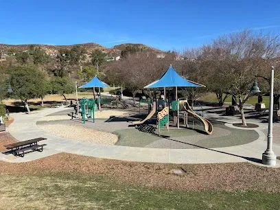 Modern playground at Todd Longshore Park with colorful climbing structures and slides, children playing under sunny skies